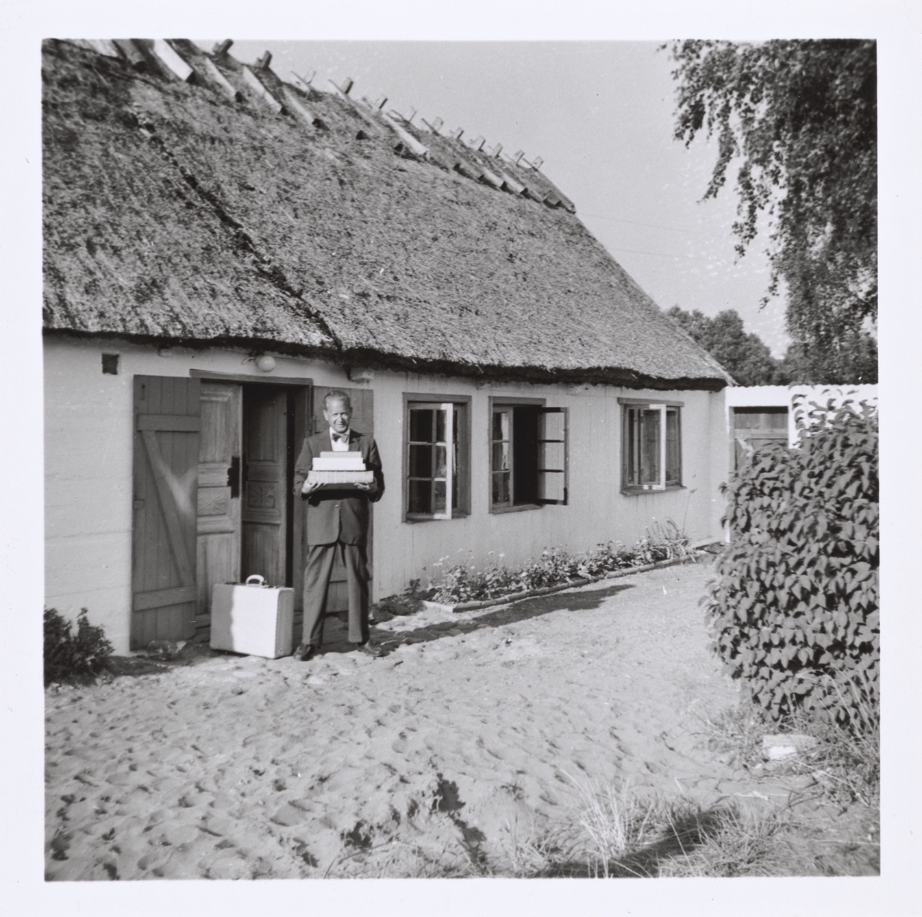 A man with a pile of books in front of a summer cottage